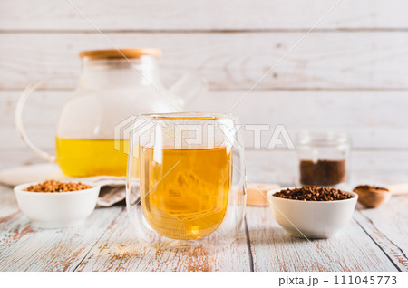 Fresh buckwheat tea in a glass and teapot and granules in a bowl on the table 111045773