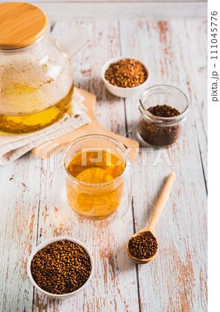 A glass of healthy buckwheat tea and granules for brewing in a bowl on the table vertical view A glass of healthy buckwheat tea and granules for brewing in a bowl on the table vertical view 111045776