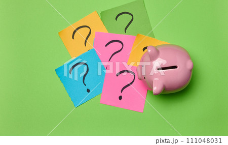 Ceramic piggy bank and stickers with drawn question marks on a green background, top view Ceramic piggy bank and stickers with drawn question marks on a green background, top view 111048031