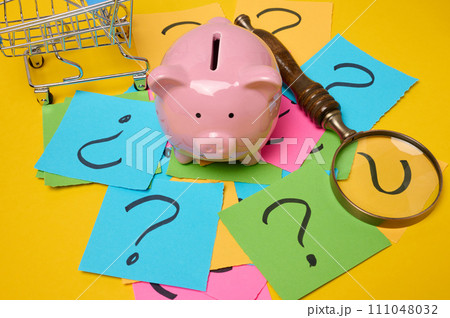Ceramic piggy bank and stickers with drawn question marks on a yellow background, top view Ceramic piggy bank and stickers with drawn question marks on a yellow background, top view 111048032