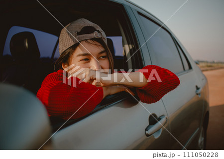 Young Asian woman leaning out of car window looking out to the field. Young Asian woman leaning out of car window looking out to the field. 111050228