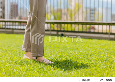 屋上の芝生の上に立つビジネスウーマンの足元 111051006