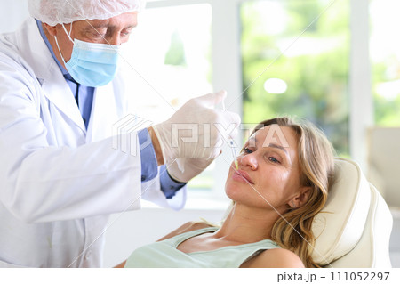 Experienced male cosmetologist doing lip fillers injections to woman 111052297