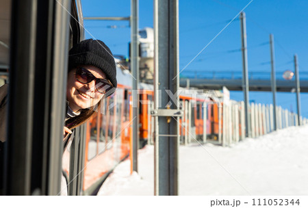 Happy woman in sunglasses sticking head out of train window passing among snowy areas 111052344