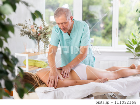 Skilled old masseur conducting back massage for woman client 111052368