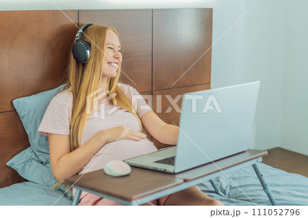 Pregnant woman working on laptop. Expectant woman efficiently works from home during pregnancy, blending professional commitment with maternal duties Pregnant woman working on laptop. Expectant woman efficiently works from home during pregnancy, blending professional commitment with maternal duties 111052796