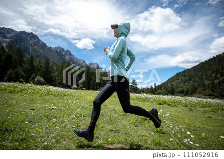 Woman trail runner cross country running in high altitude flowering mountains Woman trail runner cross country running in high altitude flowering mountains 111052916