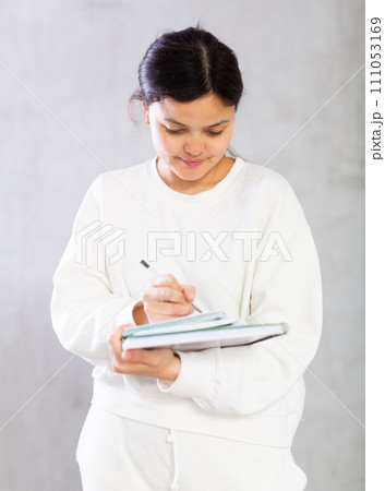 Positive young female college student writing in workbooks Positive young female college student writing in workbooks 111053169