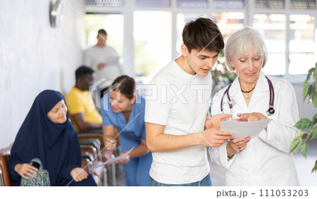 Elderly woman doctor gives document to teenager guy for signing Elderly woman doctor gives document to teenager guy for signing 111053203