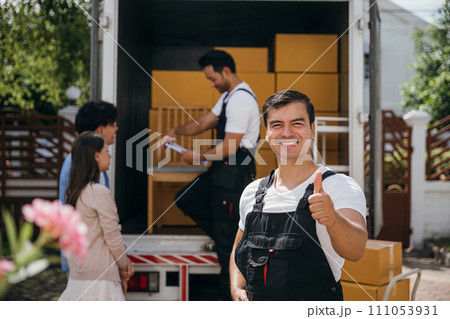 In a portrait a joyful mover unloads boxes from a truck into a new home. These movers display teamwork ensuring efficient relocation and spreading happiness. Moving day concept 111053931