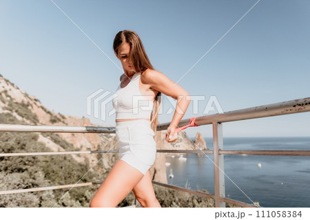 Woman sea fitness. Happy woman with long hair, fitness instructor in white doing stretching and pilates with ribbons in park near the sea. Female fitness yoga routine concept. Healthy lifestyle. Woman sea fitness. Happy woman with long hair, fitness instructor in white doing stretching and pilates with ribbons in park near the sea. Female fitness yoga routine concept. Healthy lifestyle. 111058384