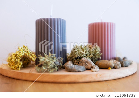 Two candles on wooden holder, stones and moss 111061838