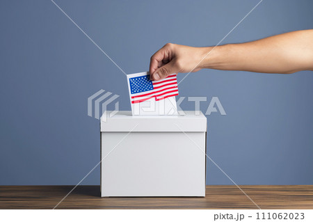 A hand inserts a ballot into a ballot box. A hand inserts a ballot into a ballot box. 111062023