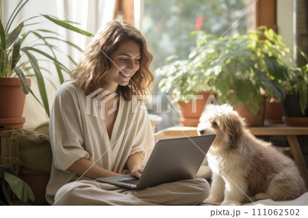 Attractive young female freelancer working on a laptop at home, with a pet dog sitting nearby. 111062502