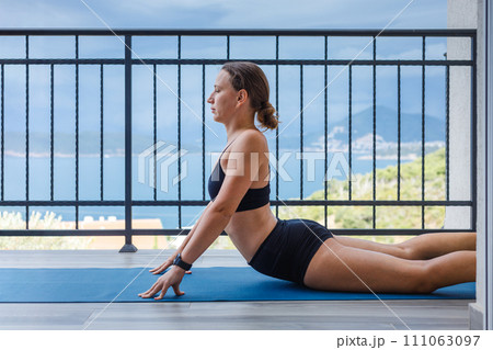 Yogi woman in sportswear in cobra pose on the mat at the balcony. Yogi woman in sportswear in cobra pose on the mat at the balcony. 111063097