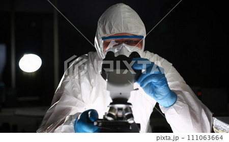 Man in protective suit looks through microscope 111063664