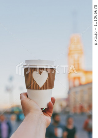 paper cup of coffee with carved white heart in women's hand on Nevsky Prospekt in St. Petersburg on sunset 111066678
