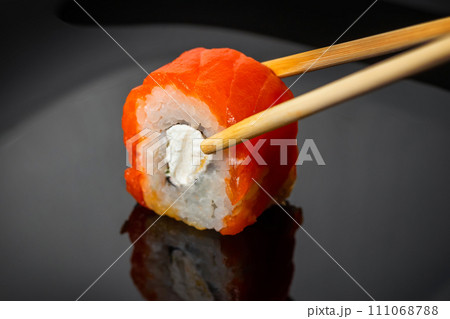 Sushi roll with salmon on a dark background, close-up Sushi roll with salmon on a dark background, close-up 111068788