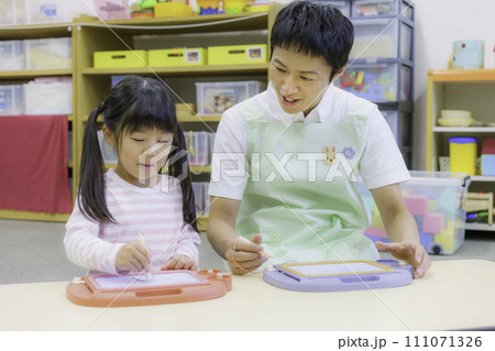 保育園でお絵描きをする笑顔の女の子と保育士さん 撮影協力:有明教育芸術短期大学 保育園でお絵描きをする笑顔の女の子と保育士さん 撮影協力:有明教育芸術短期大学 111071326
