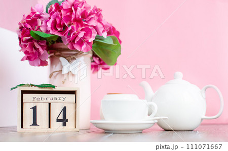 Wooden calendar with Valentine's Day for February 14 on the background of flowers and a cup of hot drink for breakfast 111071667
