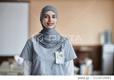 Portrait of happy Muslim woman doctor wearing gray hijab and scrubs looking at camera in medical center 111072085