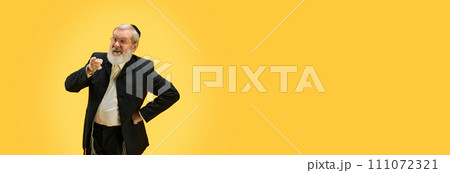 Banner. Mature man with dissatisfied look points his finger at camera against yellow studio background with negative space to inert text. 111072321
