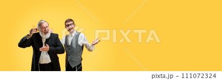 Banner. Two positive young and senior men posing in formal suits against yellow background with negative space to insert text. 111072324