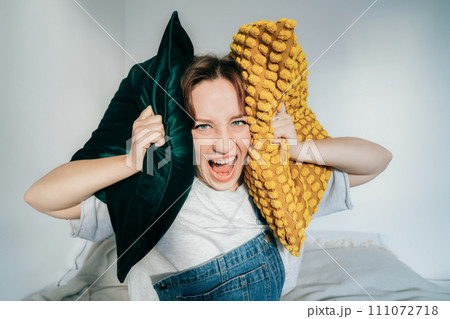 Irritated woman screaming suffers from loud noise at home covering ears with pillows annoyed by noisy neighbors, wishes silence. Angry frustrated millennial get mad hate listening disturbing noise. Irritated woman screaming suffers from loud noise at home covering ears with pillows annoyed by noisy neighbors, wishes silence. Angry frustrated millennial get mad hate listening disturbing noise. 111072718