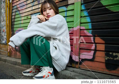 グラフィティの描かれたシャッターの前に立つ若い女性 111073565