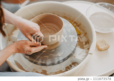 Pulling out the walls of a clay product on a potter's wheel. Hands of a Ceramist creating pottery from white clay. Close-up Pulling out the walls of a clay product on a potter's wheel. Hands of a Ceramist creating pottery from white clay. Close-up 111073578