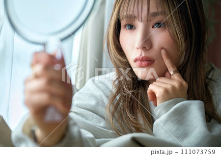 部屋で鏡を見る部屋着の若い女性 111073759