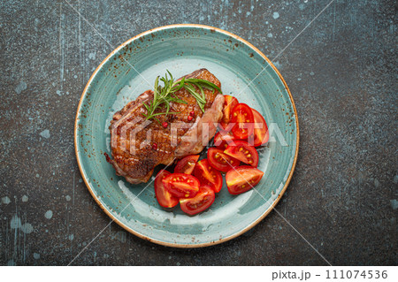 Delicious roasted duck breast fillet with golden crispy skin, with pepper and rosemary, top view on ceramic blue plate served with cherry tomatoes salad, rustic concrete rustic background 111074536