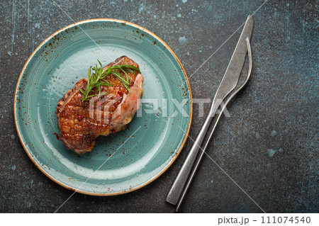 Delicious roasted duck breast fillet with golden crispy skin, with pepper and rosemary, top view on ceramic blue plate, rustic concrete rustic background 111074540