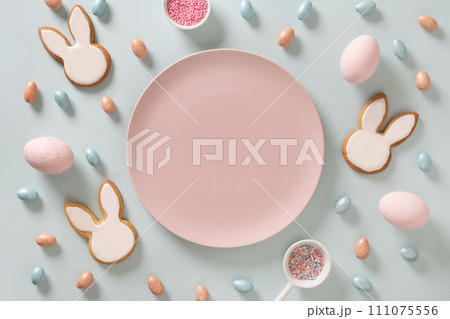 Easter homemade bunnies shaped cookies, eggs and pink plate as mock up on blue background. View from above. Festive food and snacks. Greeting card with space for text. 111075556