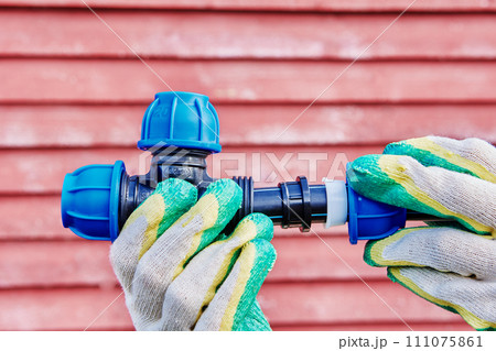 Joint tee plastic pipe fitting with section of HDPE pipe for drinking and irrigation water supply, worker hands hold structure. 111075861
