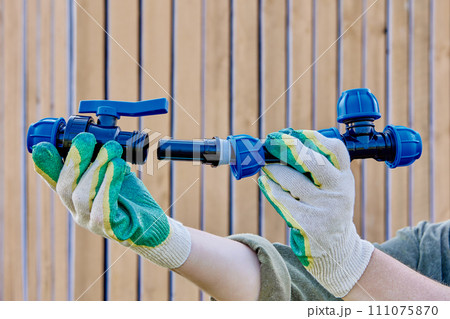 Assembly of an external water supply system using triple and valve fittings with compression threaded clamp connected by section of HDPE pipe, against background of wooden wall. Assembly of an external water supply system using triple and valve fittings with compression threaded clamp connected by section of HDPE pipe, against background of wooden wall. 111075870