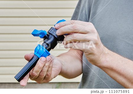 Piece of plastic pipe is inserted into compression threaded clamp of valve fitting, middle-aged Caucasian man holds joint in his hands. Piece of plastic pipe is inserted into compression threaded clamp of valve fitting, middle-aged Caucasian man holds joint in his hands. 111075891