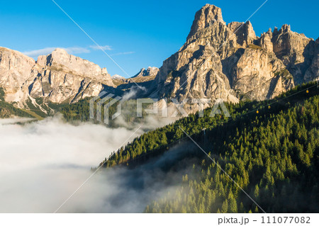Rocky peak of giant Alps rises against clear blue sky at sunrise. Dense fog envelops high mountains in a captivating aerial view on a sunny summer morning Rocky peak of giant Alps rises against clear blue sky at sunrise. Dense fog envelops high mountains in a captivating aerial view on a sunny summer morning 111077082