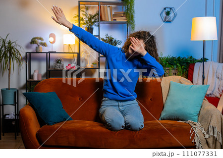 Excited young woman having fun dancing and moving to rhythm making dub dance gesture on home sofa 111077331