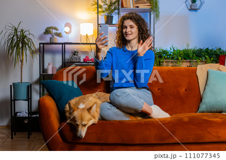 Woman taking selfie on smartphone waving hello communicating video call online recording stories Woman taking selfie on smartphone waving hello communicating video call online recording stories 111077345
