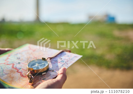 Close-up tourist's hand holds compass with magnetic arrow showing north direction, over map against lighthouse backdrop 111078210
