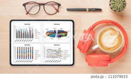 A contemporary work desk displaying a tablet with intricate business analytics, complemented by stylish eyewear, vibrant headphones, and a perfect cup of cappuccino. A contemporary work desk displaying a tablet with intricate business analytics, complemented by stylish eyewear, vibrant headphones, and a perfect cup of cappuccino. 111079633