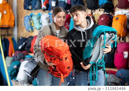 Young married couple in winter clothes chooses a durable backpack for a winter hike in tourist equipment store Young married couple in winter clothes chooses a durable backpack for a winter hike in tourist equipment store 111081486