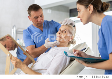 Male beautician giving consultation to woman patient with mirror in aesthetic clinic Male beautician giving consultation to woman patient with mirror in aesthetic clinic 111081538