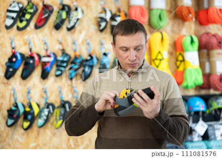 Man meticulously chooses climbing shoes in sports store 111081576