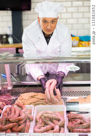 Butcher laying out raw sausages in showcase with price tags on Spanish Butcher laying out raw sausages in showcase with price tags on Spanish 111081652