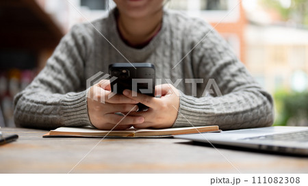 A cropped shot of a woman using her smartphone while sitting at her work desk. A cropped shot of a woman using her smartphone while sitting at her work desk. 111082308
