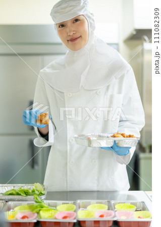 クリーンスーツでお惣菜を詰める若い女性 111082309