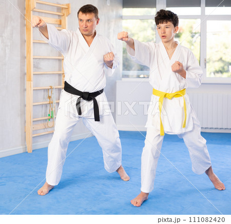 Teen boy and middle-aged man wearing kimono training karate techniques 111082420