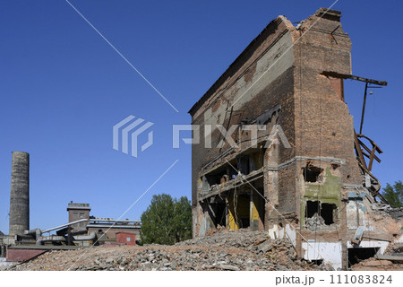 Abandoned factory with pipes, tractor, dilapidated brick buildings and walls under a clear blue sky 111083824